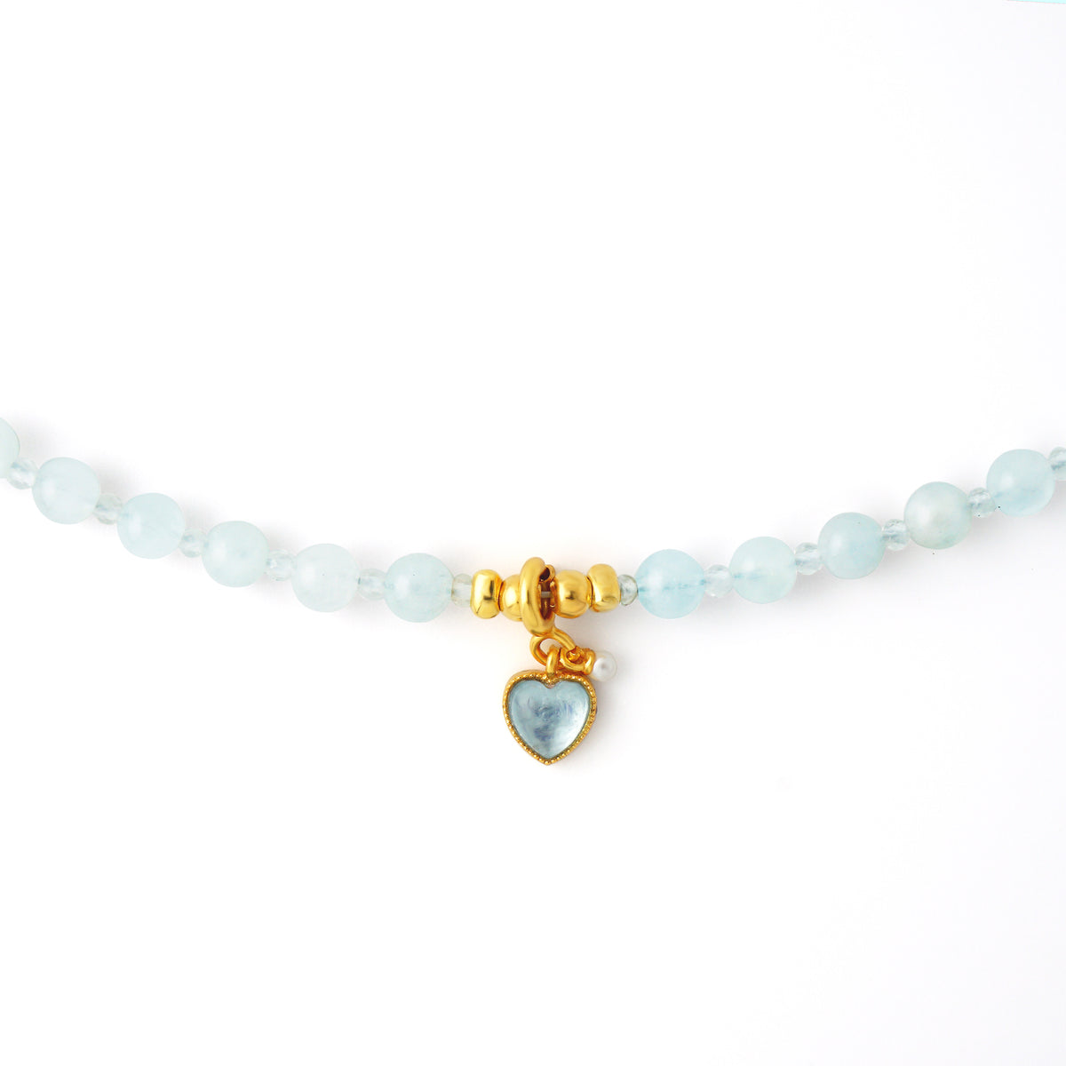 Close up detail of 18k gold plated S925 silver heart pendant with blue gemstone and pearl accent on Aquamarine beads
