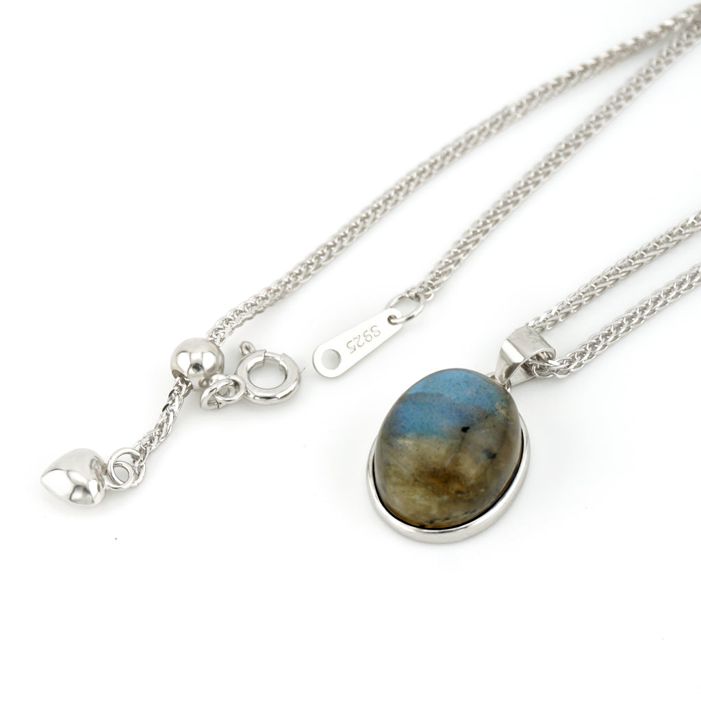A sterling silver necklace featuring an oval labradorite pendant with natural blue, brown, and gold marbling, displayed alongside its silver clasp and heart charm on a white background.