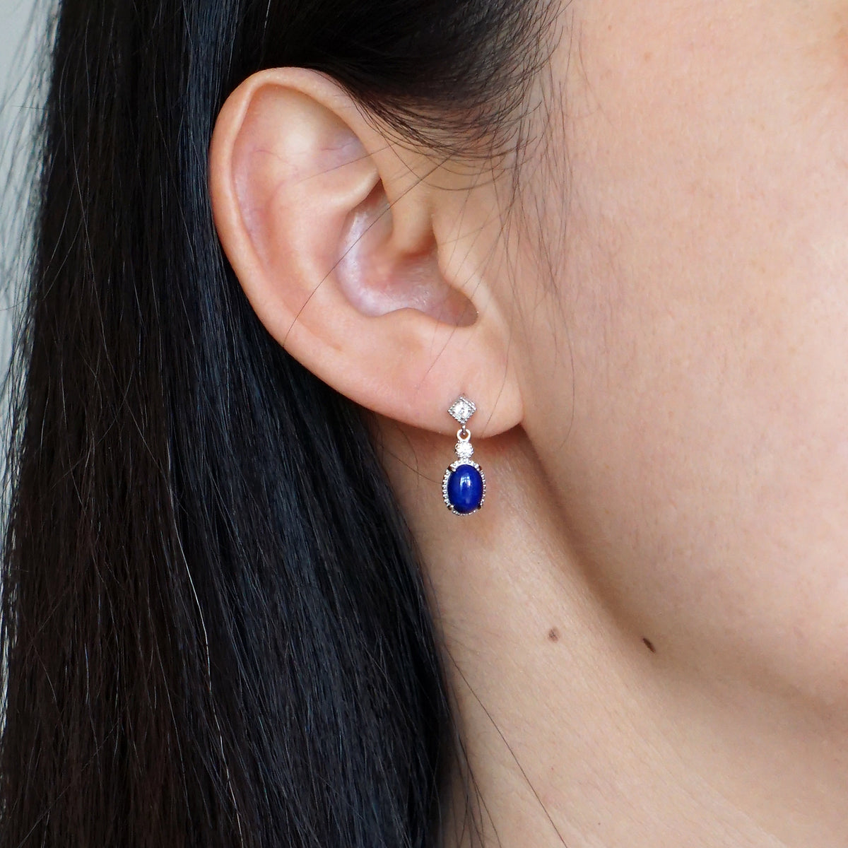 Natural deep blue oval Lapis Lazuli drop earring with CZ accents in S925 silver worn on model ear
