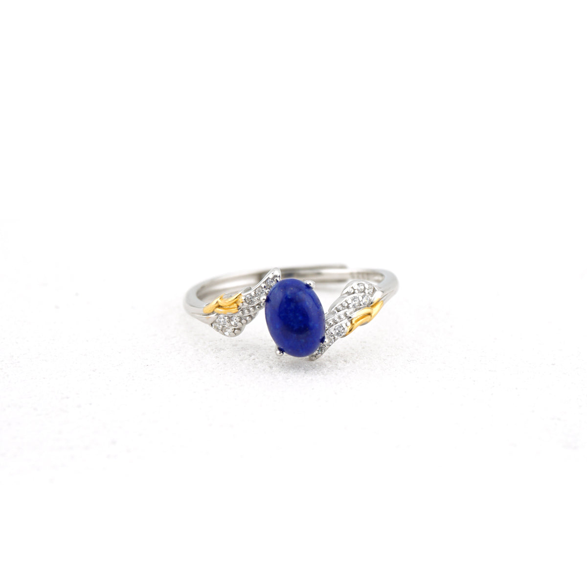 A silver and gold ring featuring an oval-cut deep blue sapphire center stone, accented by pavé-set clear crystals and small gold details on a white background.