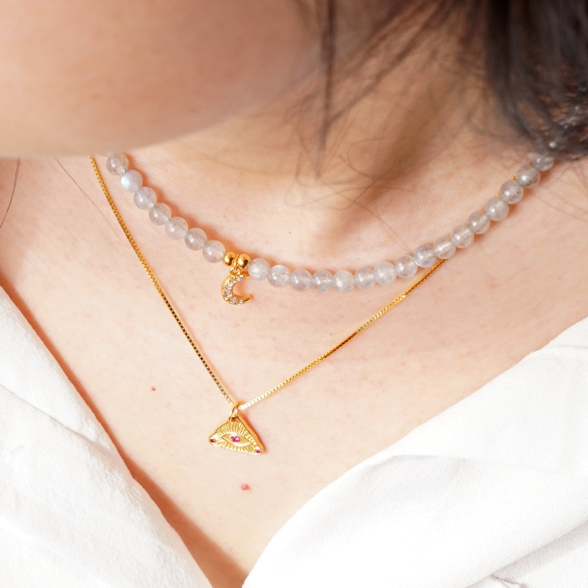 Close up view of layered Labradorite moon beaded choker and gold Evil Eye pendant necklace
