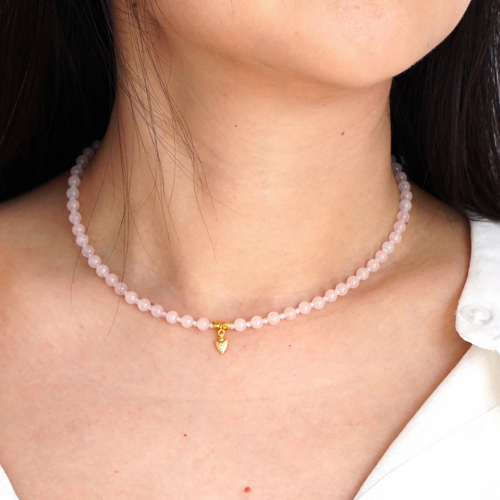 Natural pink Rose Quartz beaded choker necklace with gold arrow pendant worn on model neck
