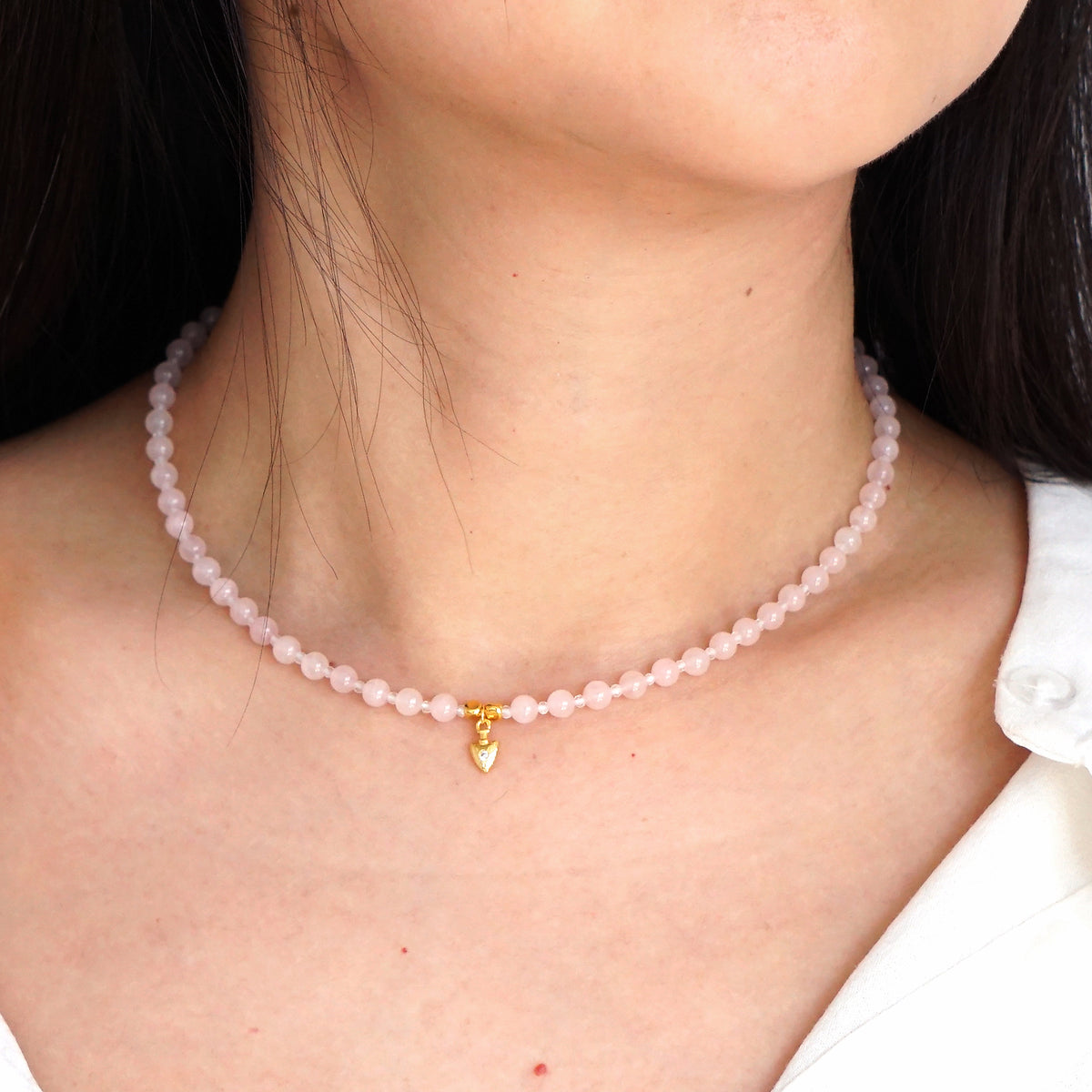 Natural pink Rose Quartz beaded choker necklace with gold arrow pendant worn on model neck

